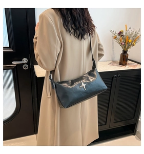 Chic black glossy leather shoulder bag with silver star detail worn by model indoors