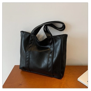 Detail of a vintage black leather tote bag with a decorative front pocket on wood
