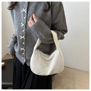 Detailed close-up of white corduroy shoulder bag with model wearing a grey knitted cardigan