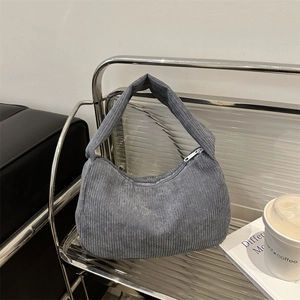 Blue corduroy shoulder bag with crescent shape and silver zipper on a metal rack