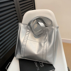 Silver metallic large capacity tote bag with wide straps on a minimalist chair