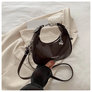 Close-up of a dark brown crescent hobo bag with glossy finish and silver clover charm