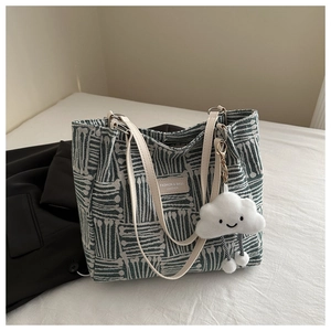 Detail of striped canvas tote with leather straps and a plush cloud charm accessory