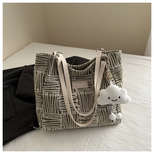 Close-up of green striped tote bag with leather tag and white plush smiley charm
