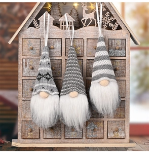 Close-up of three knitted grey and white Christmas gnomes hanging on a wooden calendar