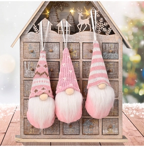 Close-up of three pink knitted Christmas gnomes hanging on a wooden advent calendar