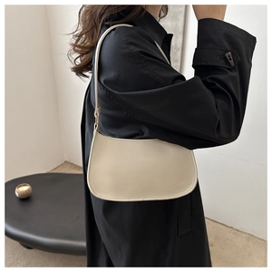 Close-up of minimalist beige hobo bag on shoulder against black trench coat