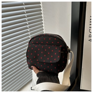Detail of a black and red heart patterned crossbody bag with adjustable white strap