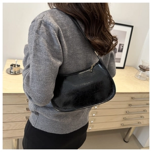 Détail d'un sac hobo noir brillant avec zip doré porté à l'épaule dans un décor minimaliste