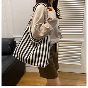 Detail of a large black and white striped canvas tote bag worn on a woman's shoulder