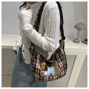 Dettaglio di una borsa hobo a quadri marroni con toppa a cucciolo indossata a spalla