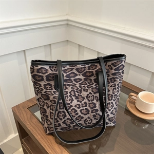 Stylish large leopard print tote bag with black leather straps on a wooden table