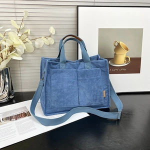 Blue corduroy tote bag with large front pockets and adjustable strap on a wood surface