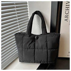 Detail view of the black puffer tote bag showing quilted texture and snap button closure
