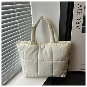 Detail of cream quilted tote bag showing large grid stitching and matte button closure