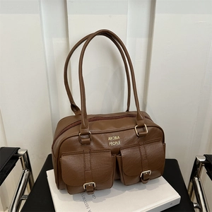 Brown leather tote bag with double handles and front buckled pockets on a white stand