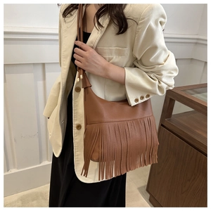 Close-up of caramel leather tote bag with retro tassels and adjustable strap on a model
