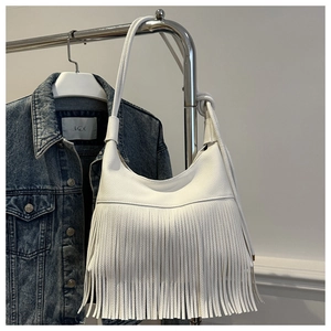 Detalle del bolso hobo blanco con flecos y correa con nudo sobre fondo de tela vaquera