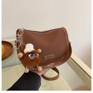 Dettaglio borsa vintage in pelle marrone con ciondolo di peluche e zip metallica