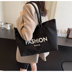 Detalle de bolso tote de lona negra con letras Fashion Paris y correa de cuero