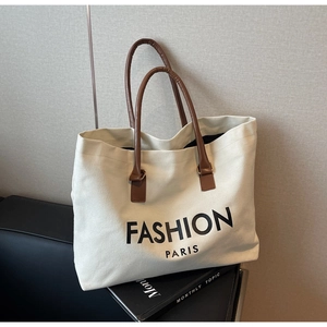 Detail of canvas tote bag with leather handles resting on a black leather chair
