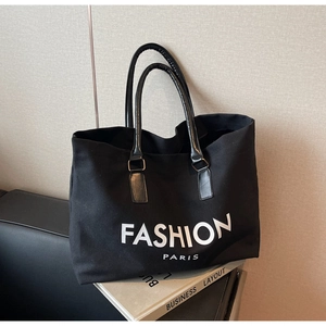 Detail of black canvas tote bag showing the fashion lettering and faux leather handles