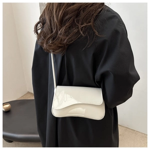 Detailed view of cream patent leather underarm bag with unique wavy flap and slim strap