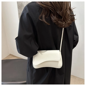 Chic white leather shoulder bag featuring unique wave-shaped flap design on black coat