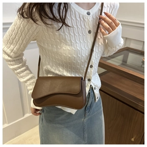 Detail of a brown matte leather crossbody bag with a unique wavy asymmetrical flap design