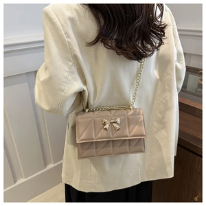Détail du sac bandoulière matelassé beige avec boucle nœud doré porté par mannequin