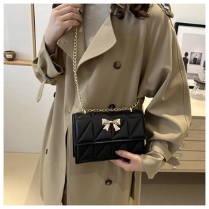 Détail du sac matelassé noir avec fermoir papillon doré porté sur un trench-coat kaki