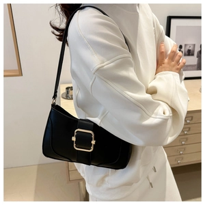 Detail of classic black underarm bag with gold buckle on a model in a white sweatshirt