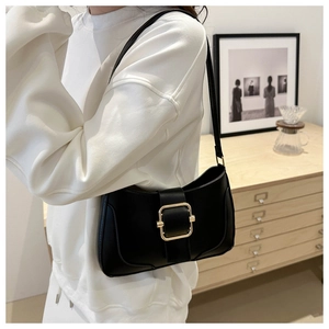 Classic black leather underarm bag with a large gold square buckle on a model in a cozy room
