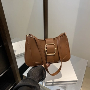 Brown leather underarm bag with gold square buckle shown in a stylish lifestyle setting
