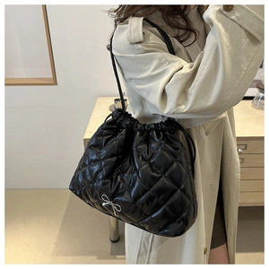 Detail of black quilted drawstring tote bag with a silver bow charm on a beige trench coat