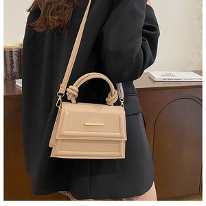 Detail of minimalist beige crossbody bag with knotted handle and sleek metal fastener