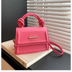 Close-up of fuchsia crossbody bag with knotted handle and golden metal trim on lid