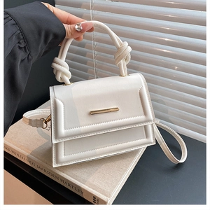 Close-up of stylish white handbag with knotted handle and elegant gold metal clasp