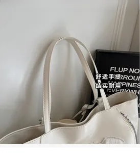 Close-up of durable cream faux leather tote bag handles and side zipper with plush charm