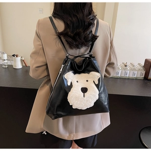 Detail of black PU leather backpack featuring a plush dog applique worn by a model