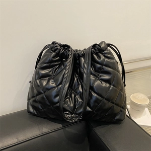 Quilted black drawstring tote bag with diamond pattern on leather sofa setting