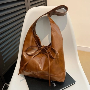 Brown vintage oil wax leather shoulder bag with a bow tie detail on a white chair