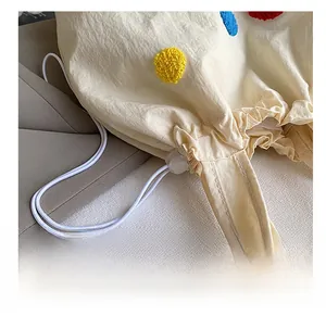 Détail du sac à cordon blanc avec pompons colorés et fermoir de réglage en plastique
