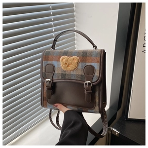 Close-up of checkered fabric backpack with leather trim and cute plush bear embroidery