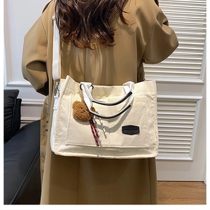 Detail of white corduroy tote bag featuring a cute plush bear charm and fabric strap