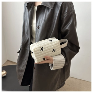Detail of quilted makeup clutch featuring black bow patterns and a side strap