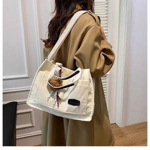 White corduroy tote bag detail with fashion label, bear charm and ribbon on model