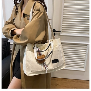 Detail of cream corduroy tote bag with plush bear charm and adjustable shoulder strap