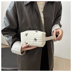 Detail of white quilted cosmetic bag featuring black bow embroidery and wide woven handle