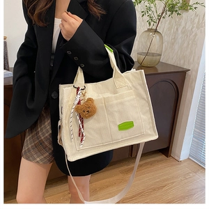 Detail of off-white corduroy tote bag showing textured pockets and bear charm